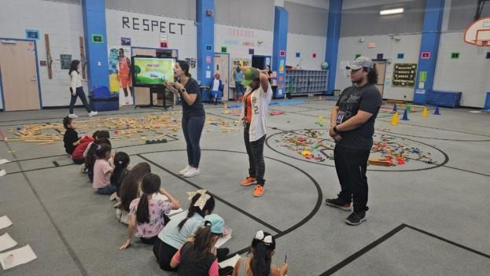 Students sitting on floor in school gym being instructed by CATCH staff.